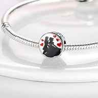 Charm argenté représentant un couple dansant entouré de petits cœurs rouges, sur bracelet serpent argenté.
