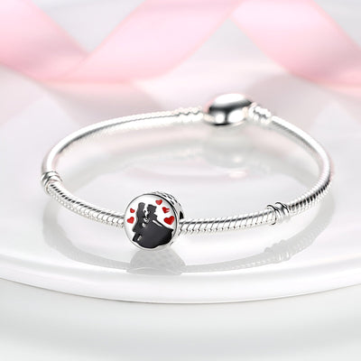 Bracelet argenté avec charm couple dansant en silhouette noire et détails rouges sur fond blanc.