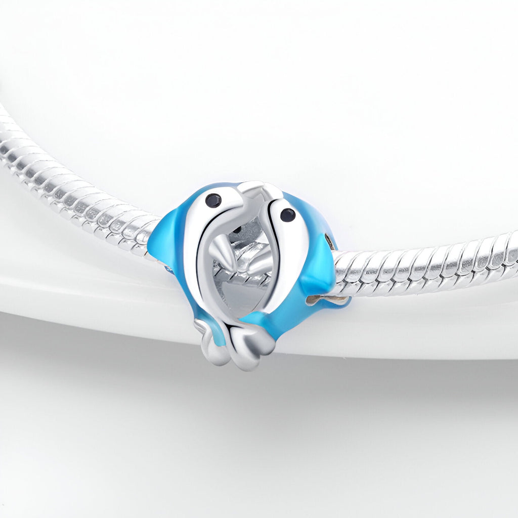 Charm argenté duo de dauphins bleus s'enlaçant sur bracelet serpent argenté.