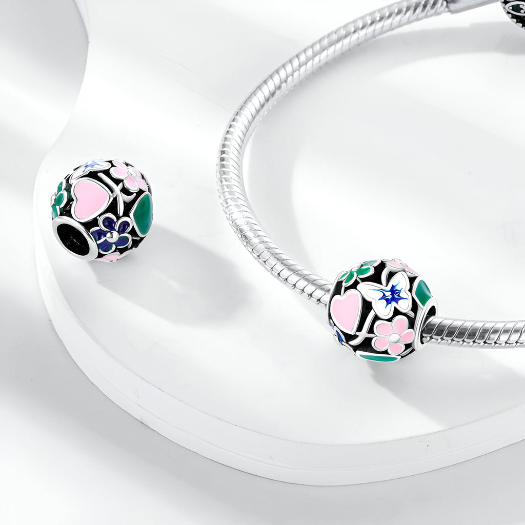 Charm rond noir avec motifs fleurs roses, bleues et papillon, finition argentée brillante.