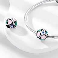 Charm rond noir avec motifs fleurs roses, bleues et papillon, finition argentée brillante.