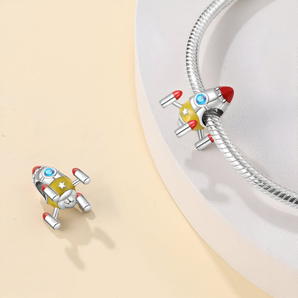 Charm fusée spatiale en métal argenté avec détails rouges et bleus sur bracelet serpentine.