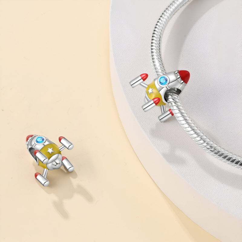 Charm fusée spatiale en métal argenté avec détails rouges et bleus sur bracelet serpentine.