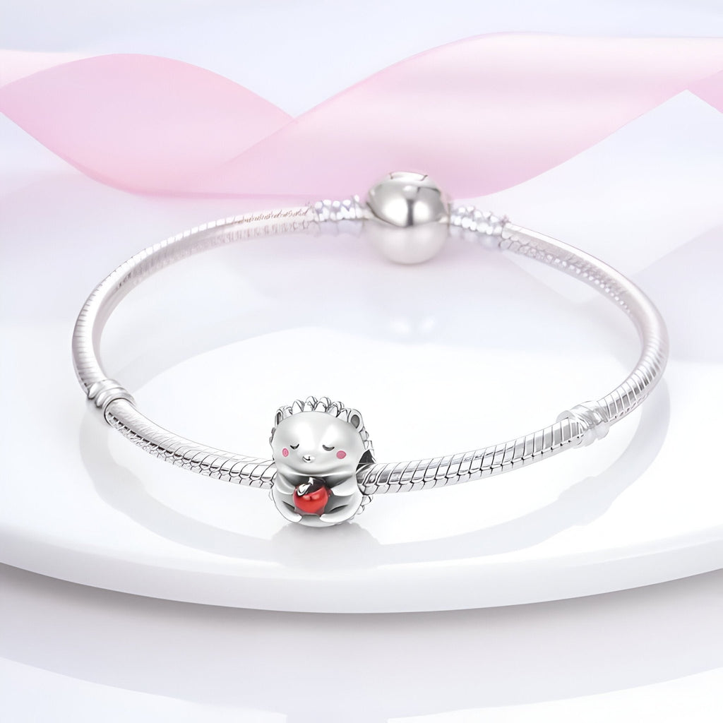 Bracelet argent avec charm hérisson détaillé tenant un cœur rouge brillant.