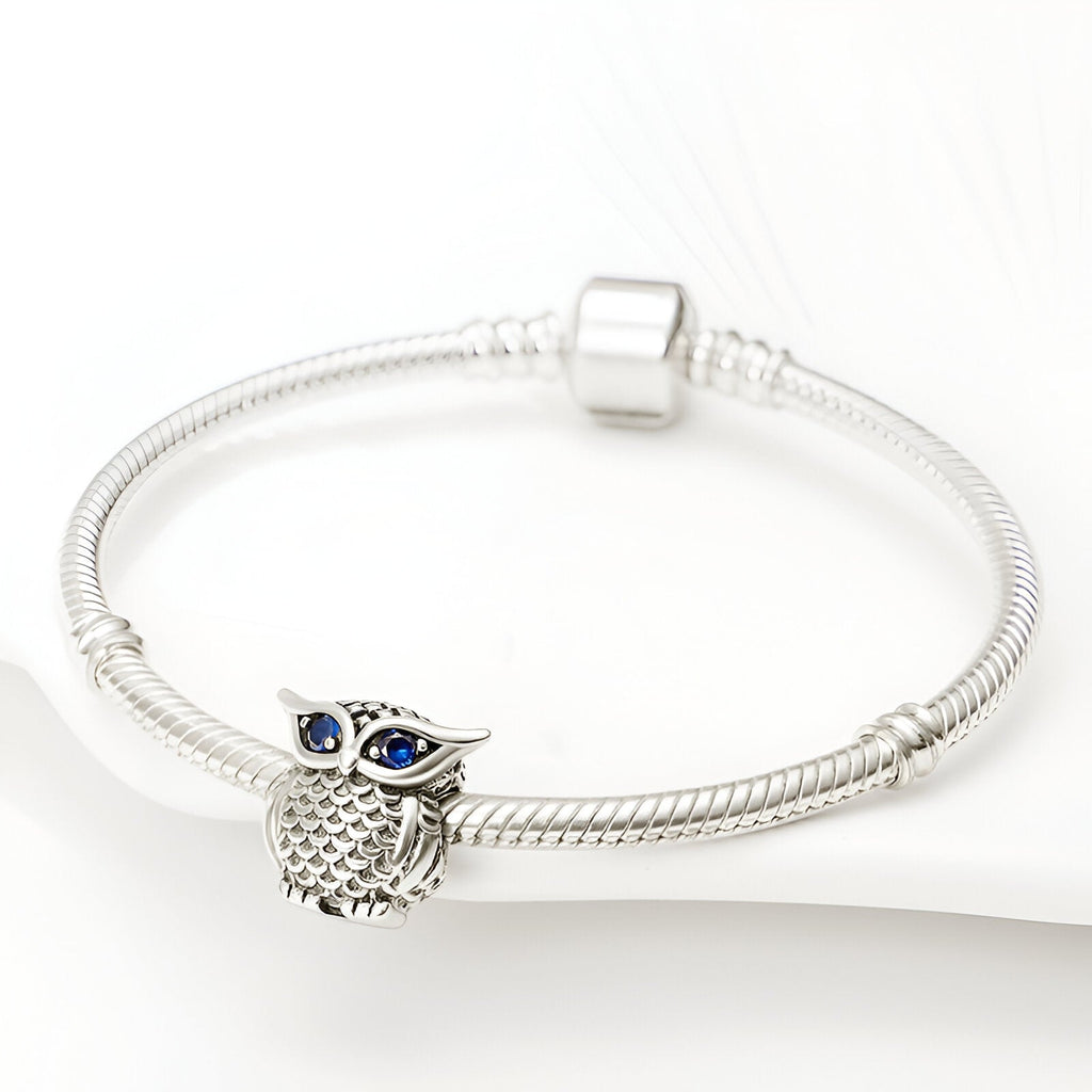 Bracelet argenté avec charm hibou détaillé aux yeux bleus en forme de perles.