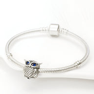 Bracelet argenté avec charm hibou détaillé aux yeux bleus en forme de perles.