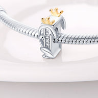 Charm lettre I en argent orné de petites pierres blanches avec couronne dorée sur un bracelet serpent argenté.