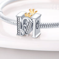 Charm lettre M en argent avec détails en strass et petite couronne dorée sur bracelet serpent en métal.