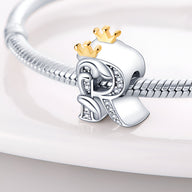 Charm lettre R en argent orné de petits cristaux, avec une couronne dorée sur le dessus.