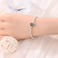 Bracelet argent fin avec charm lune serti de pierres vert foncé sur poignet féminin.