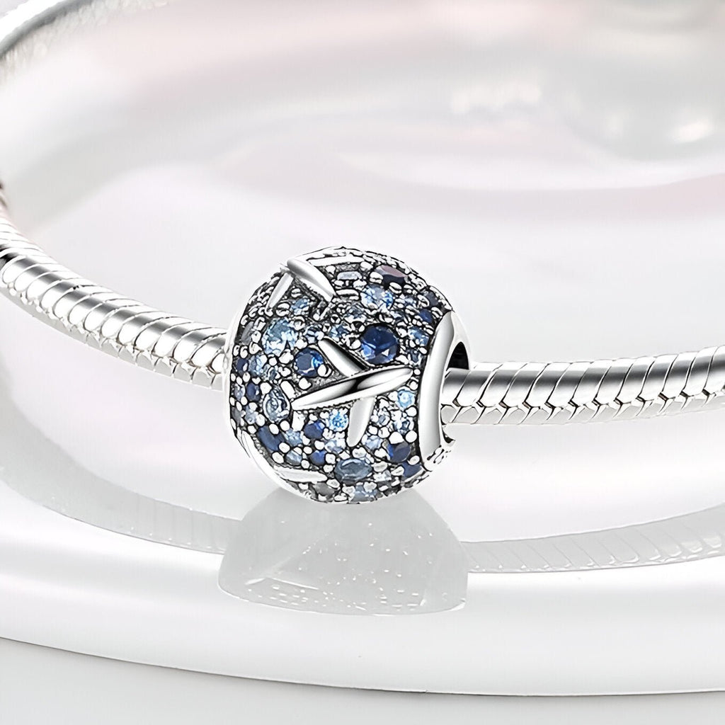 Charm rond argenté orné de petits avions et de pierres bleues sur bracelet serpent argenté.