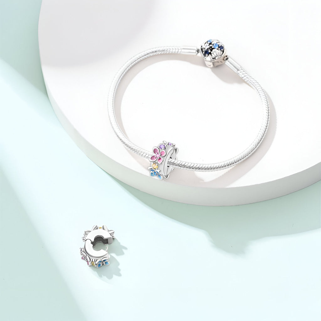 Charm bracelet en argent avec multiples fleurs colorées et perle bleue sur cordon fin.