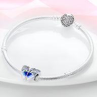 Bracelet argenté avec charm papillon orné de strass bleus et détails ajourés.