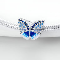 Charm papillon argenté avec strass bleus et dégradé bleu sur les ailes, monté sur un bracelet serpent.