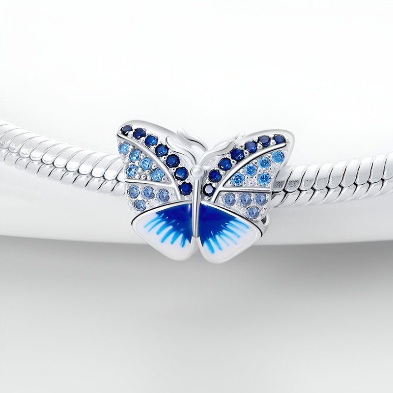 Charm papillon argenté avec strass bleus et dégradé bleu sur les ailes, monté sur un bracelet serpent.