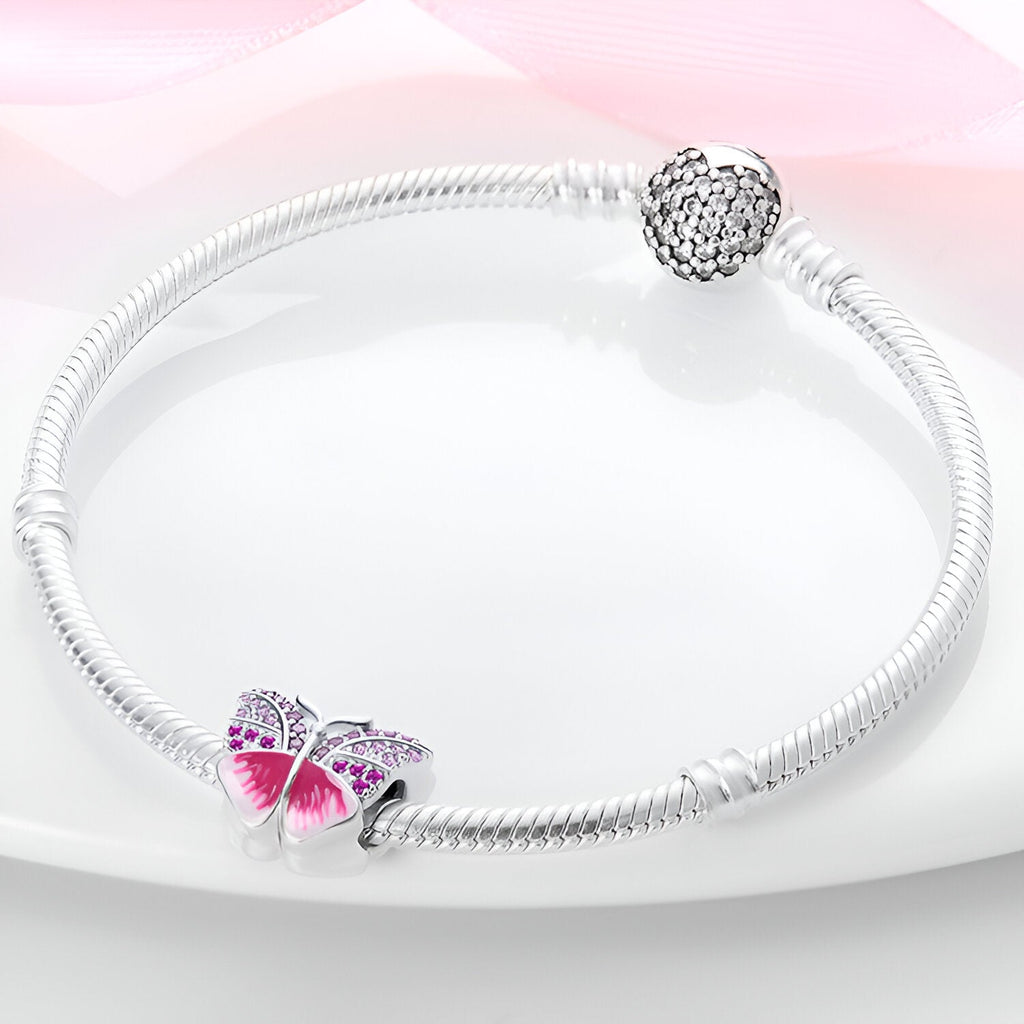 Bracelet argenté avec un charm papillon rose délicatement détaillé.