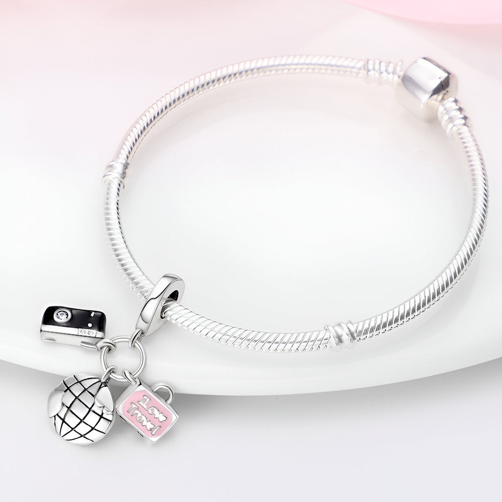 Bracelet argenté à mailles serpent avec pendentifs globe, appareil photo et valise rose pâle.