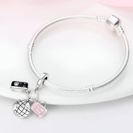 Bracelet argenté à mailles serpent avec pendentifs globe, appareil photo et valise rose pâle.