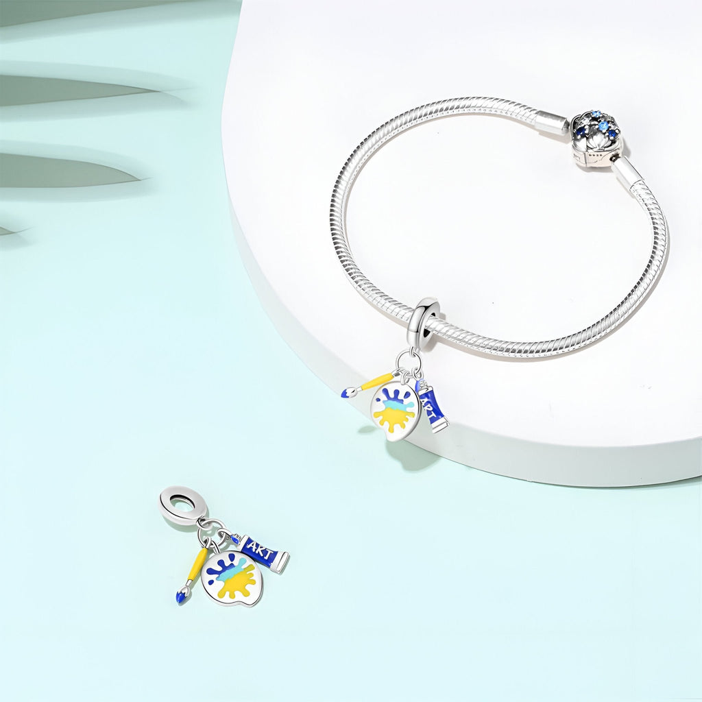 Bracelet argenté avec pendentif charm peint en blanc, jaune et bleu, motif artistique.