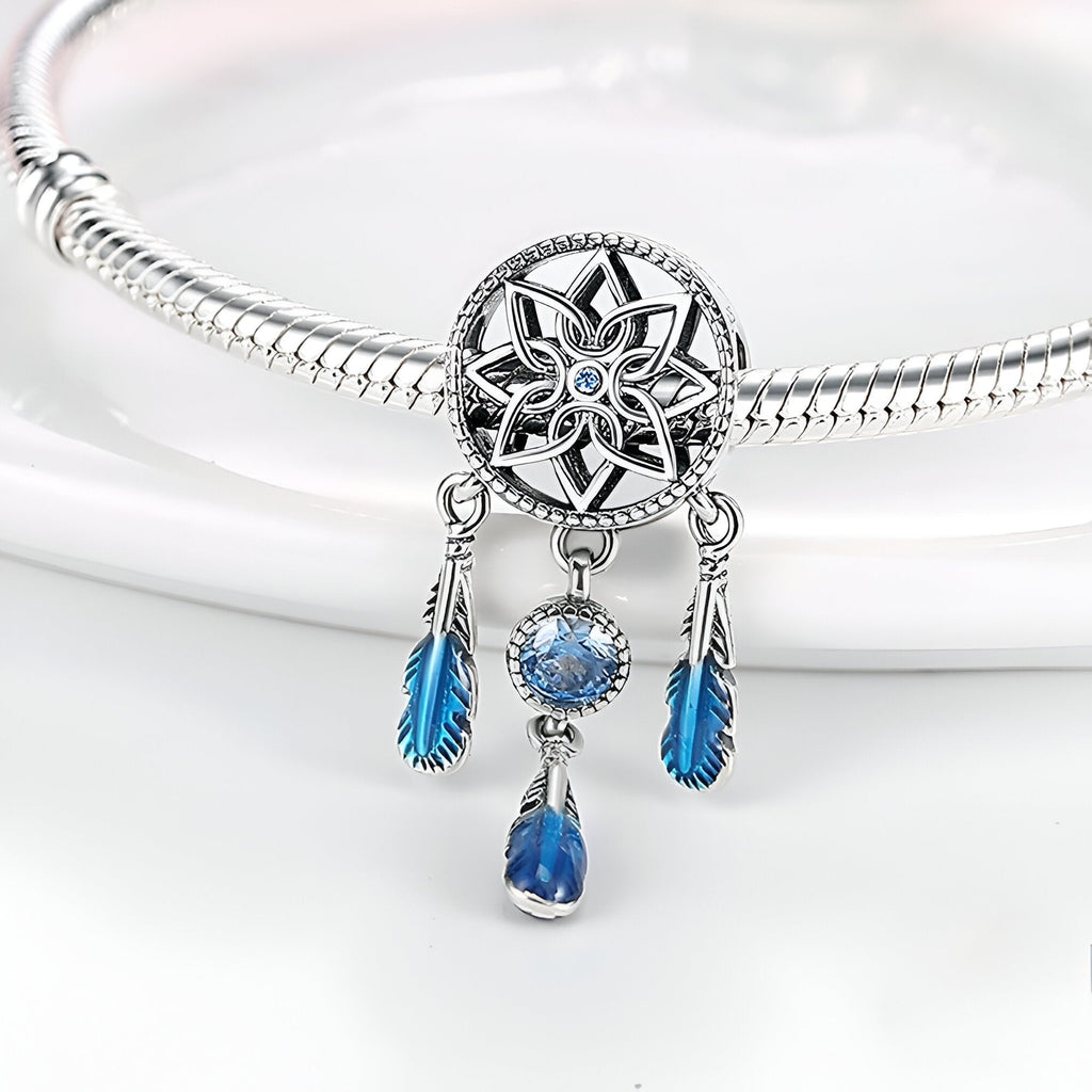 Charm pendentif attrape-rêves argent avec pierres bleues et plumes suspendues sur bracelet serpent.