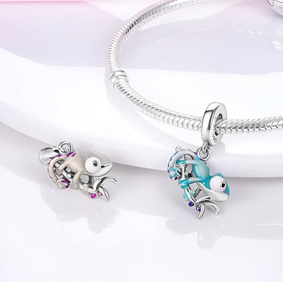 Charm caméléon argent avec détails rose et turquoise, pendentif suspendu à un bracelet serpent argenté.