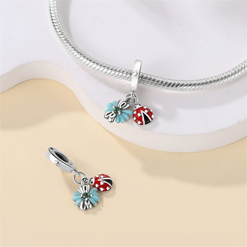 Charm pendentif argenté avec une coccinelle rouge et une feuille bleue émaillées, style délicat.