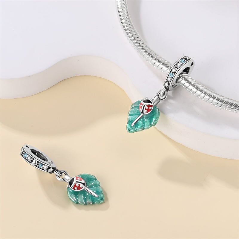Charm pendentif avec coccinelle rouge sur feuille verte émaillée, attache argentée avec pierres bleues.