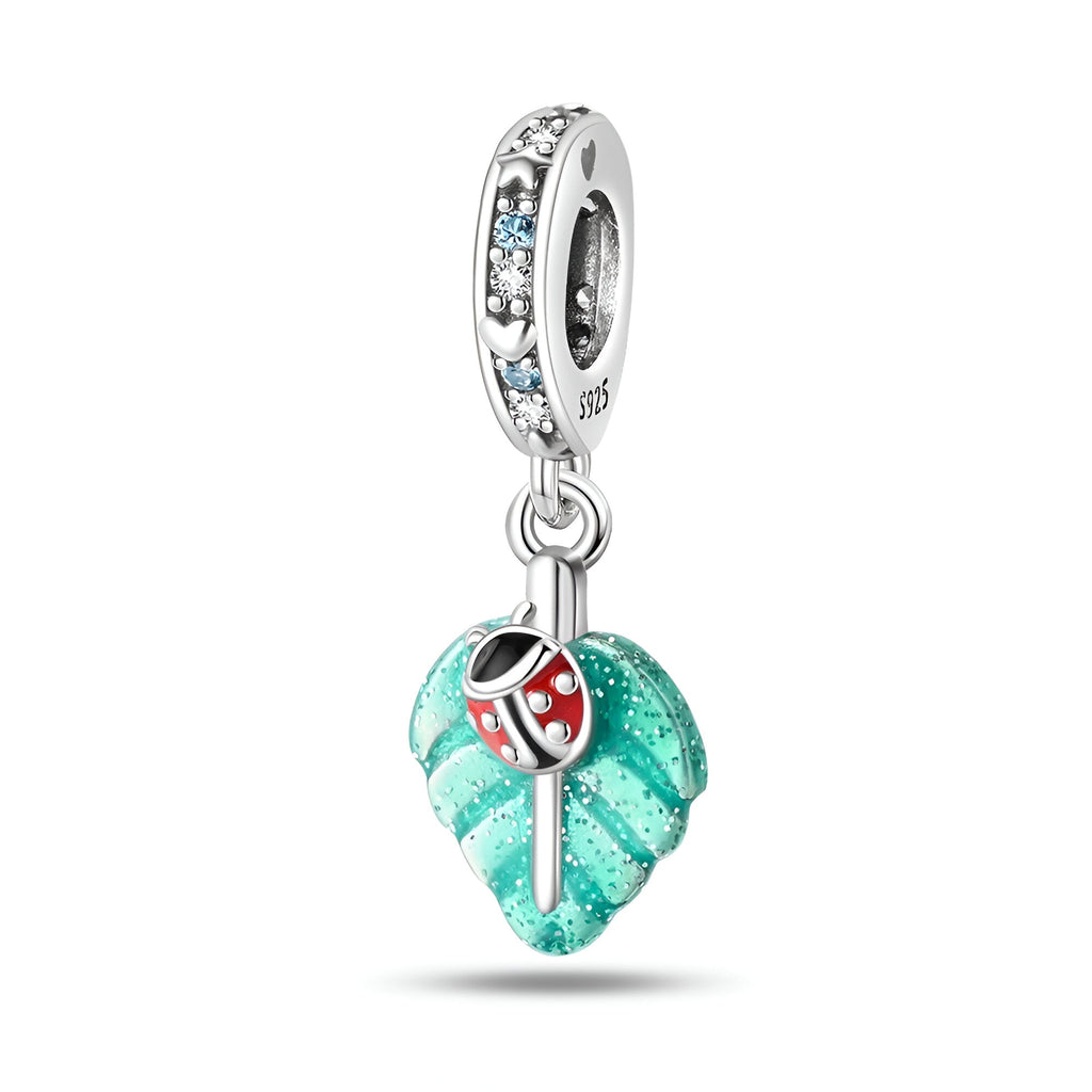 Pendentif charm argent coccinelle rouge sur feuille turquoise texturée avec anneau orné de pierres bleues.