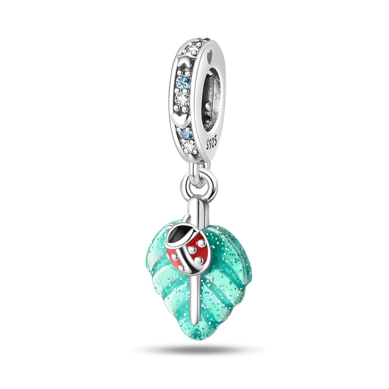 Pendentif charm argent coccinelle rouge sur feuille turquoise texturée avec anneau orné de pierres bleues.
