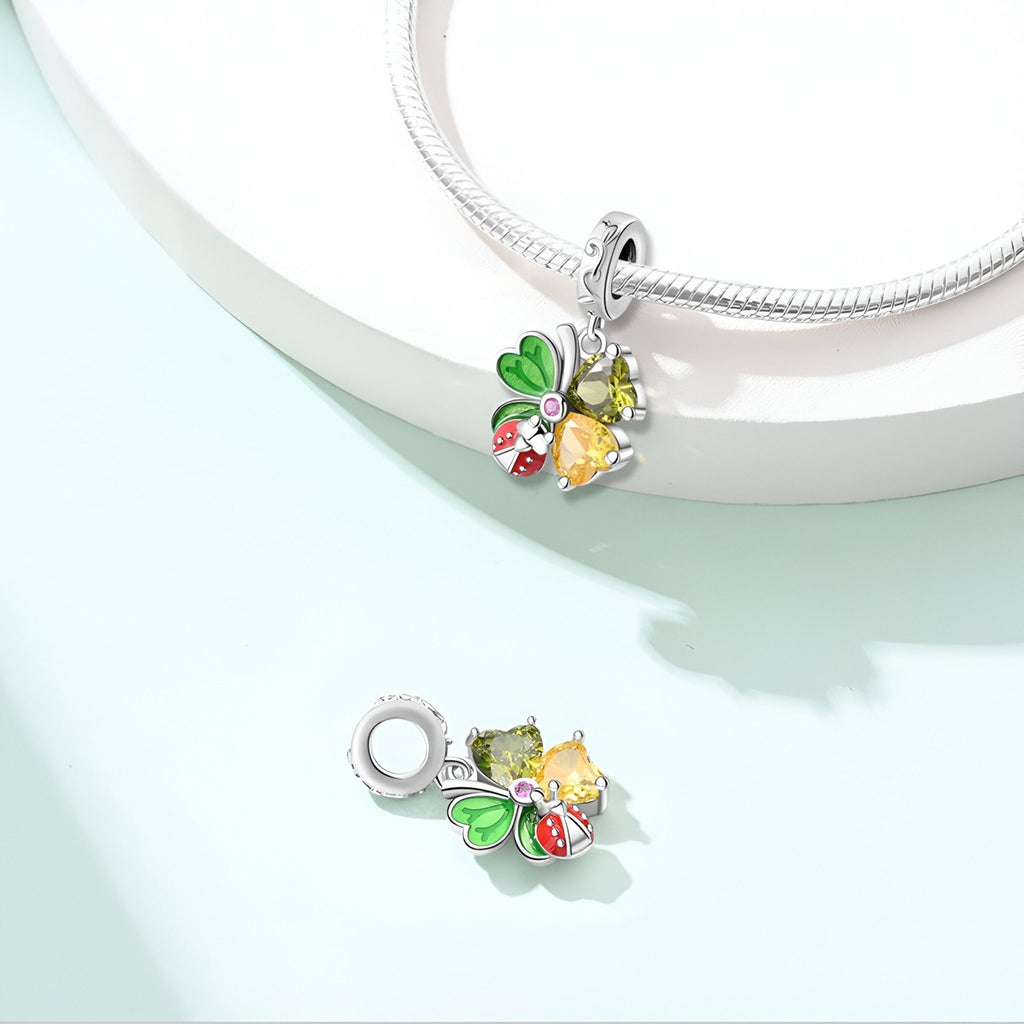 Pendentif charme argent coccinelle rouge sur trèfle vert avec détail papillon jaune.