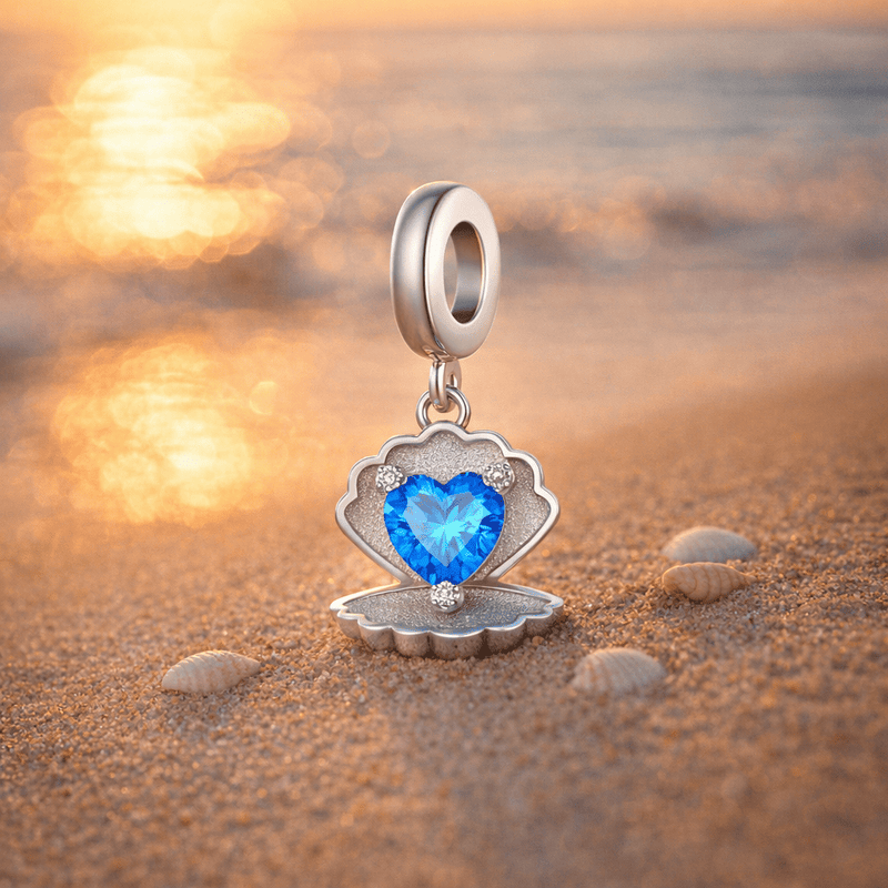Charm Conchilia coquillage cœur bleu posé sur le sable doré au coucher du soleil avec petits coquillages