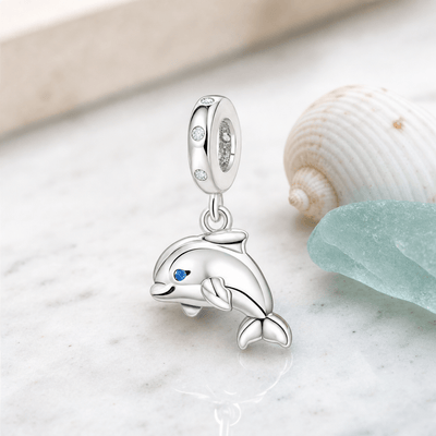 Charm pendentif dauphin argent posé sur marbre blanc avec coquillage et verre de mer