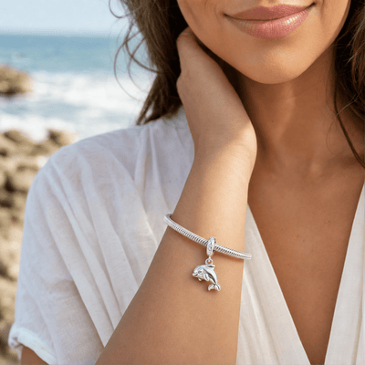 Charm dauphin argent porté sur un bracelet au poignet d'une femme en bord de mer