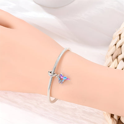 Bracelet argent fin avec pendentif oiseau et papillon coloré sur poignet féminin.