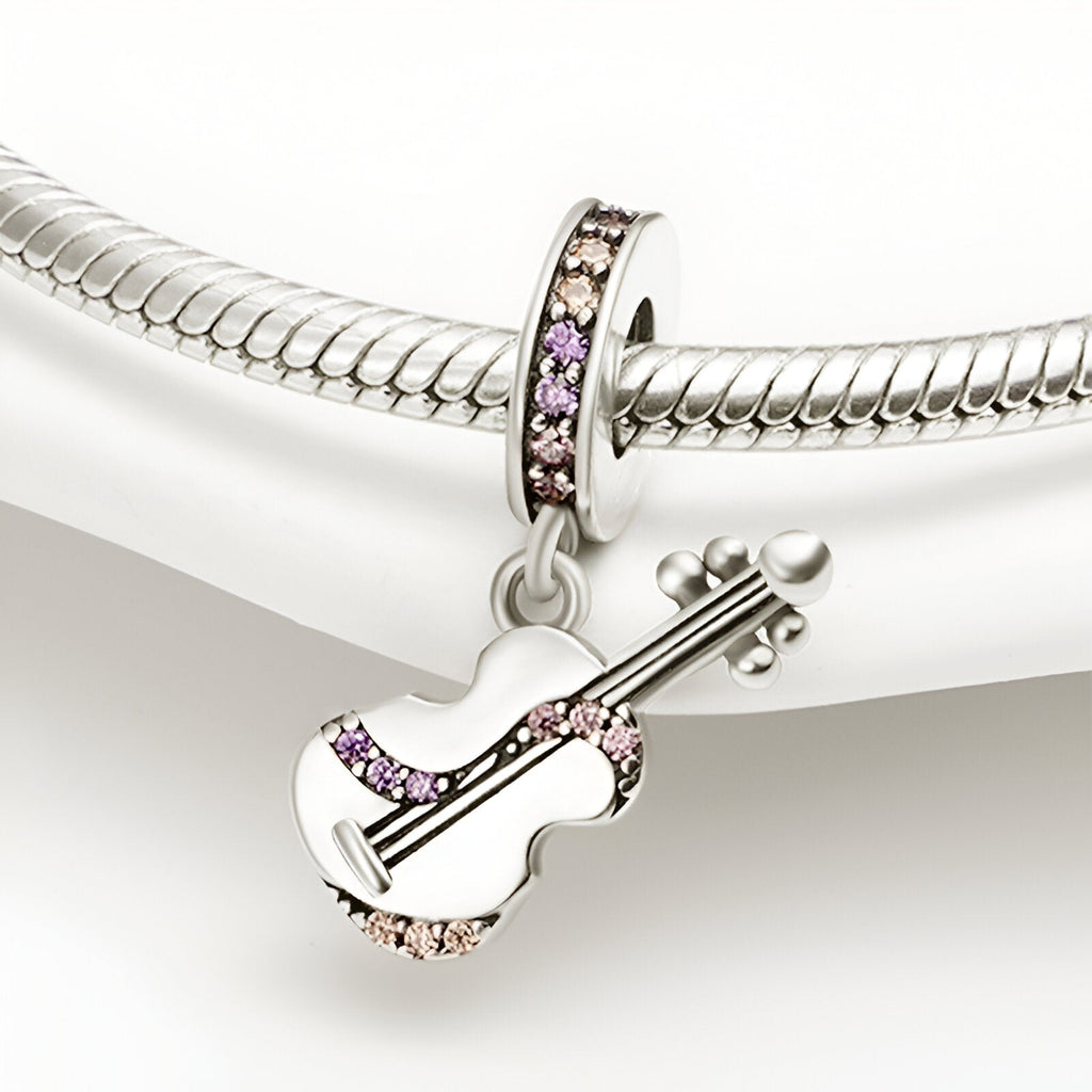 Pendentif guitare en métal argenté avec détails en strass rose et lilas suspendu à un bracelet serpent argenté.