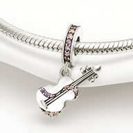 Pendentif guitare en métal argenté avec détails en strass rose et lilas suspendu à un bracelet serpent argenté.