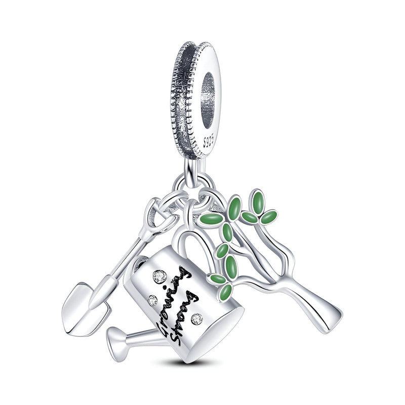 Pendentif charm argenté avec arrosoir, pelle de jardinage et petite branche aux feuilles vertes.