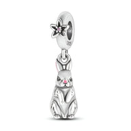 Charm pendentif lapin assis en argent avec détails roses et fleur ajourée sur l’anneau.