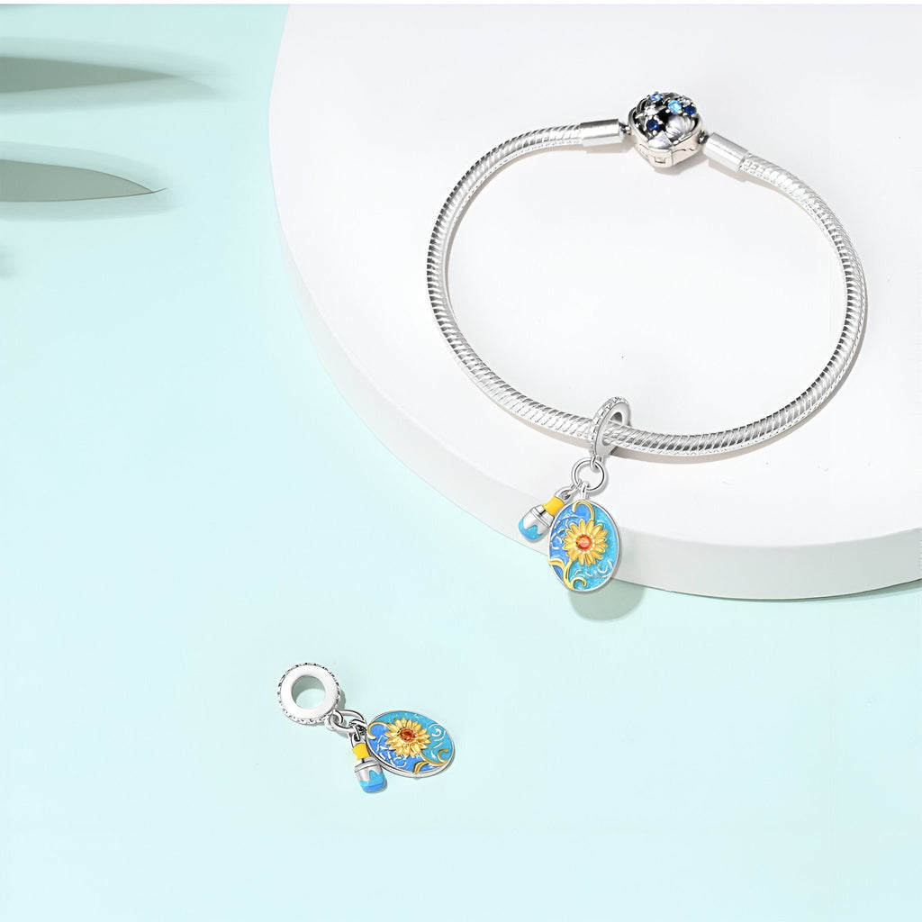 Bracelet argenté avec pendentif charm tournesols colorés bleu et jaune sur fond blanc.