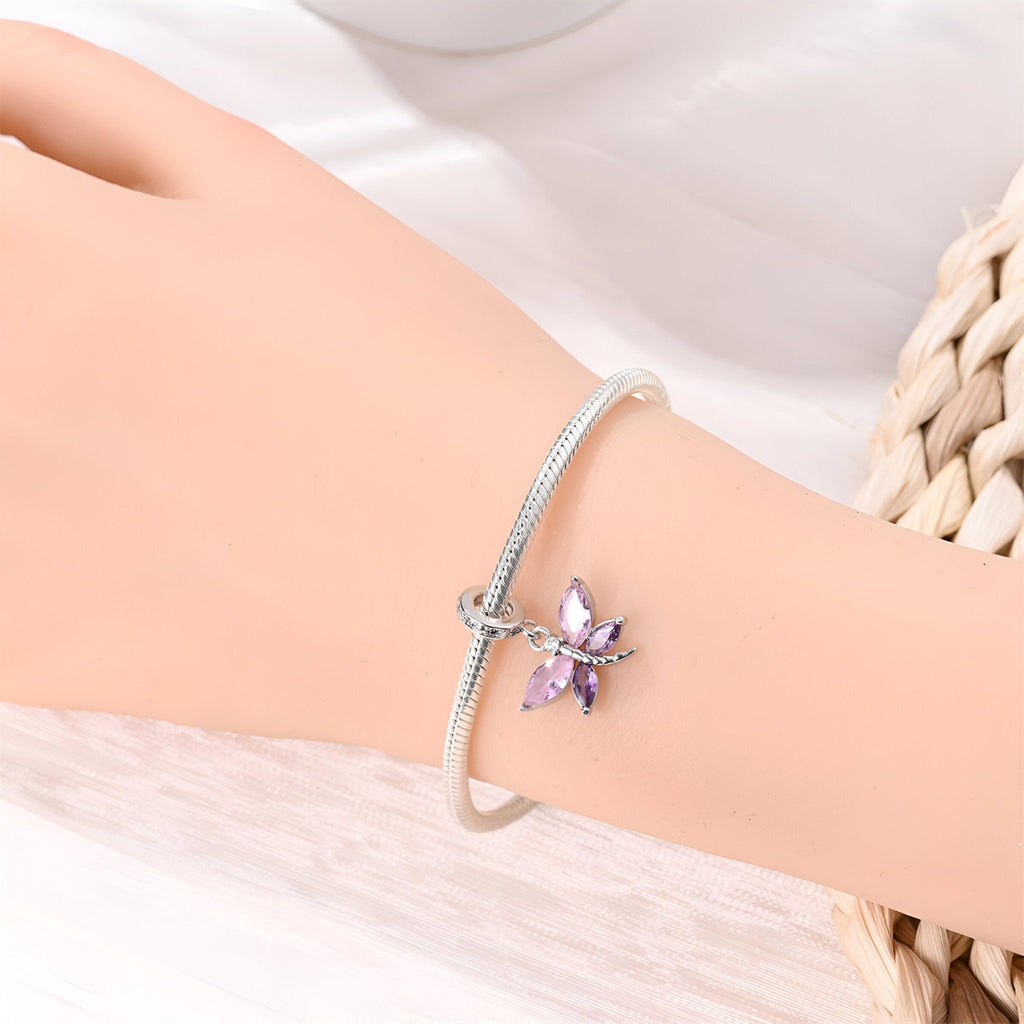 Bracelet argenté avec pendentif libellule violet et ailes détaillées sur poignet féminin.