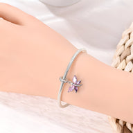 Bracelet argenté avec pendentif libellule violet et ailes détaillées sur poignet féminin.