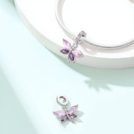 Pendentif libellule argenté avec ailes roses translucides sur collier serpent argenté.