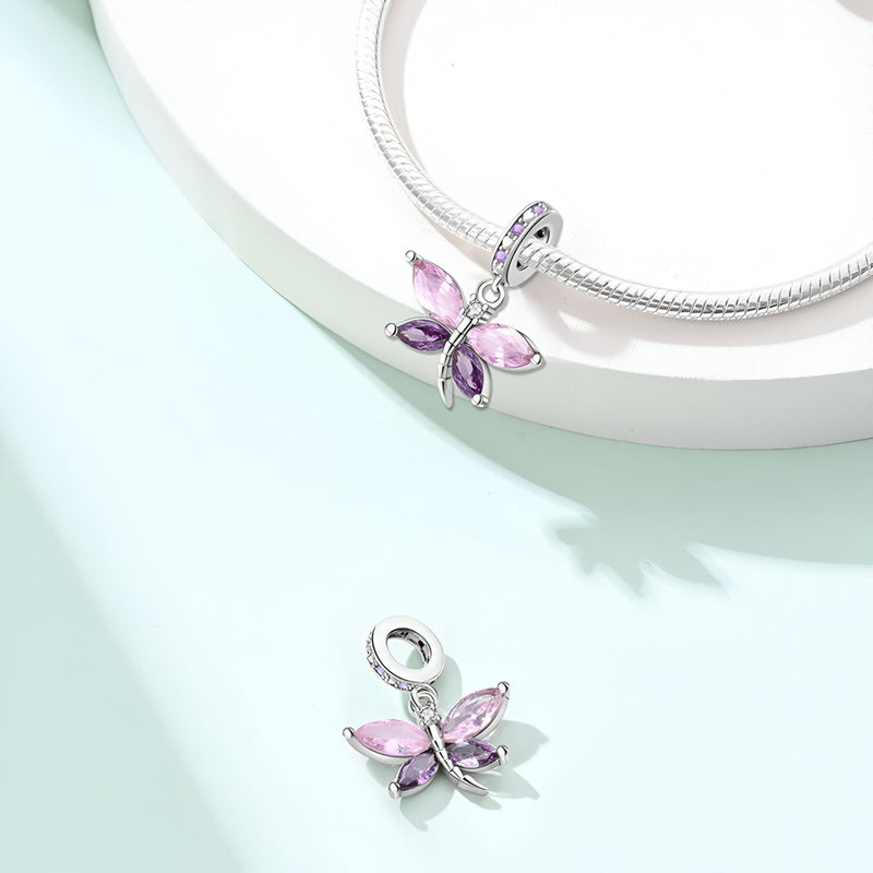 Pendentif libellule argenté avec ailes roses translucides sur collier serpent argenté.