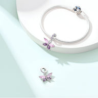 Bracelet argenté avec pendentif libellule rosée violet orné de cristaux colorés et fermoir à bille bleu.