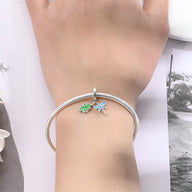Bracelet argenté avec pendentifs libellule bleue et feuille verte émail sur poignet féminin.