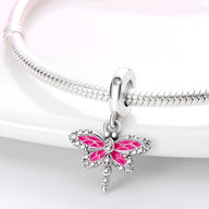 Charm pendentif libellule rose en argent avec ailes émaillées et strass, suspendu à un bracelet serpent argenté.