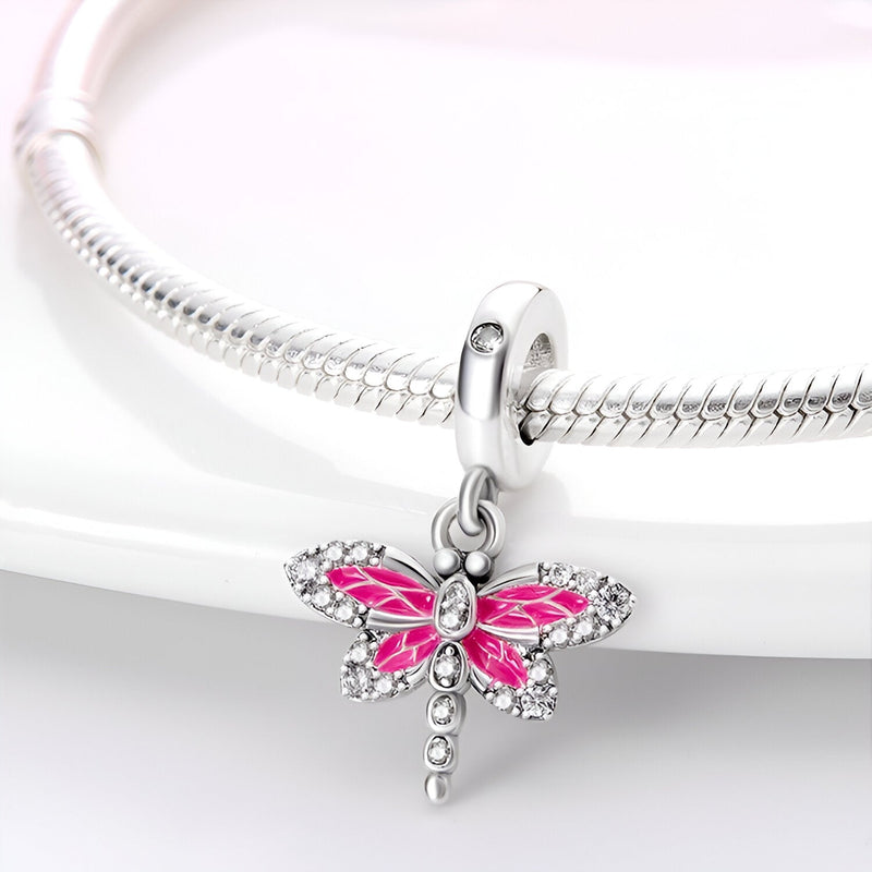 Charm pendentif libellule rose en argent avec ailes émaillées et strass, suspendu à un bracelet serpent argenté.