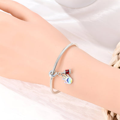 Bracelet argenté avec pendentif main remplie de peinture multicolore et petit drapeau rouge et noir.