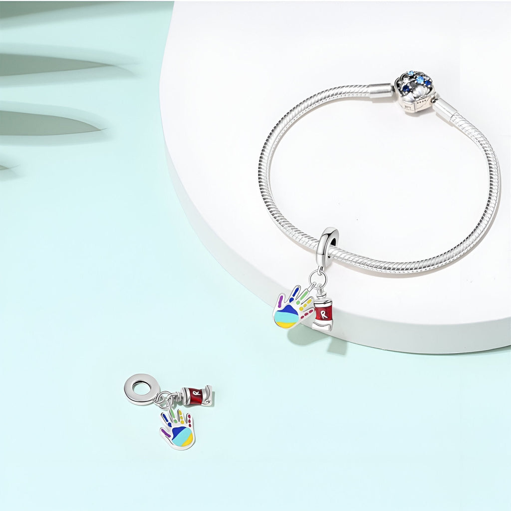 Bracelet argent avec pendentif main colorée remplie de peinture et petit tube de peinture en métal rouge.