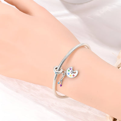 Bracelet argenté avec pendentif palette de peinture colorée et pinceau finement détaillé.